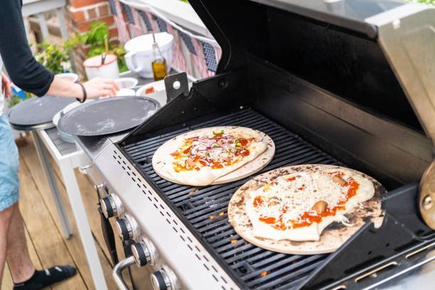 Preparing individual grilled pizzas on an outdoor gas grill.
